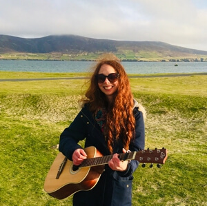 Jo playing guitar outdoors by the sea